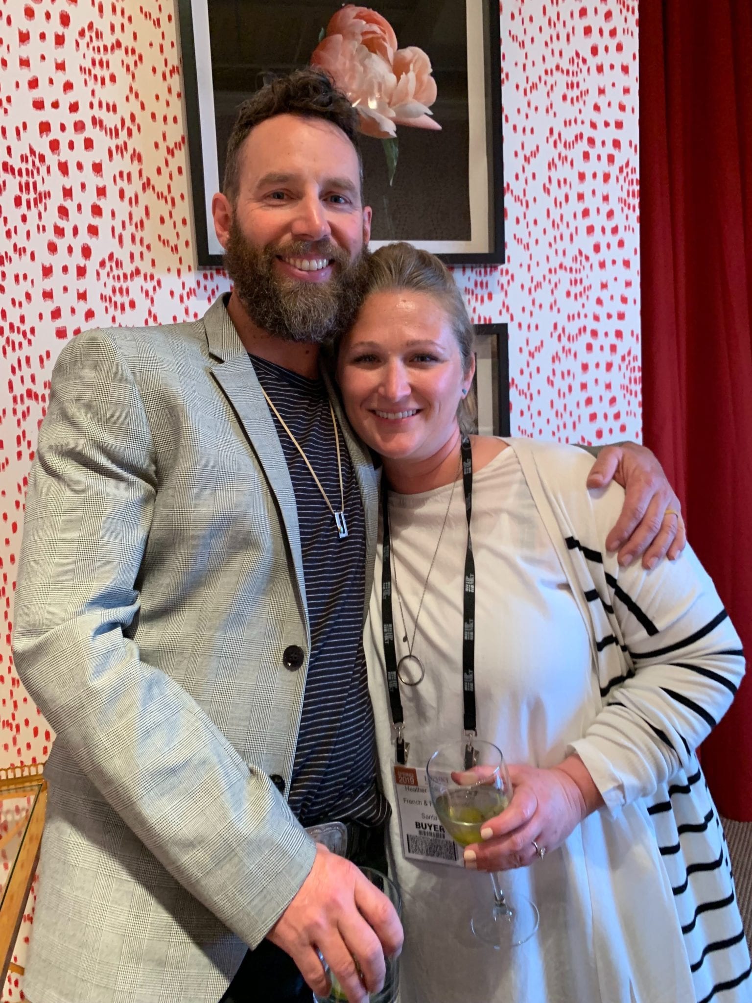 Matt and Heather French posing for a photograph in a room with red spotted wallpaper and framed artwork of a rose